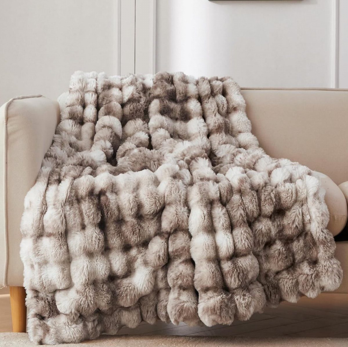 Fluffy beige and brown faux-fur blanket draped over a neutral colored sofa.