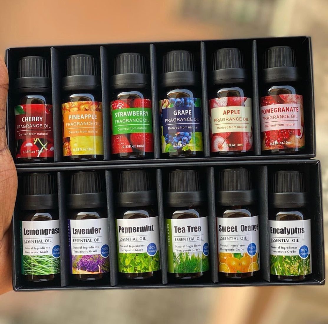 Twelve small amber oil bottles in a black gift box held by hand.