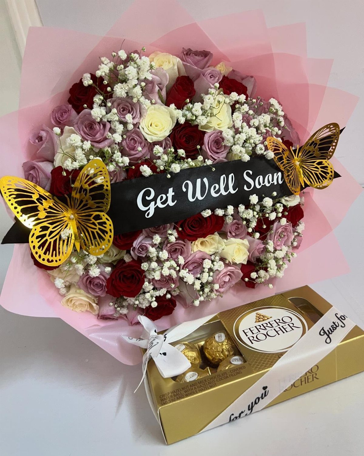 Floral arrangement of red and pink roses with gold butterflies and chocolates.