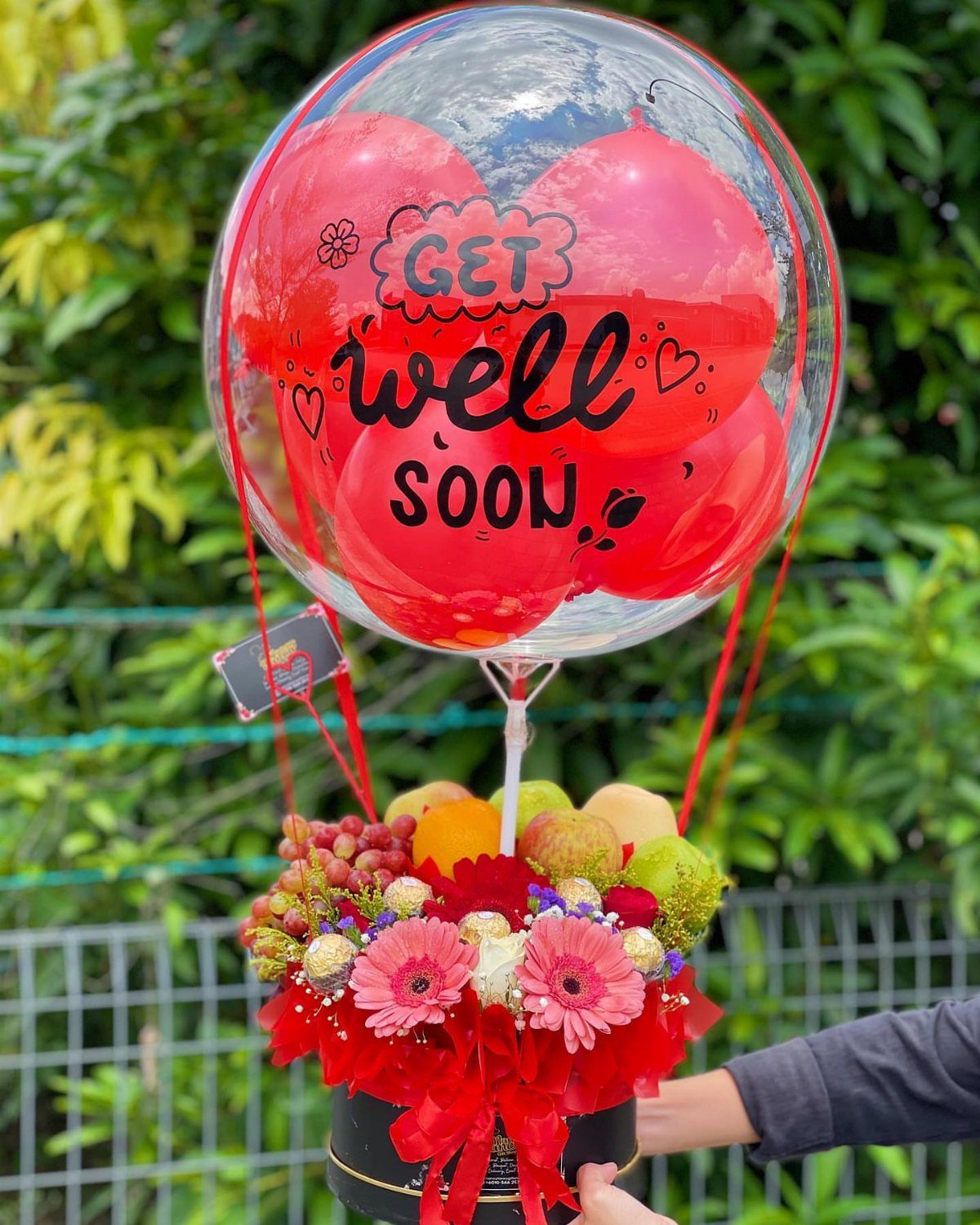 Get well soon balloon floating over a fruit and flower gift basket.