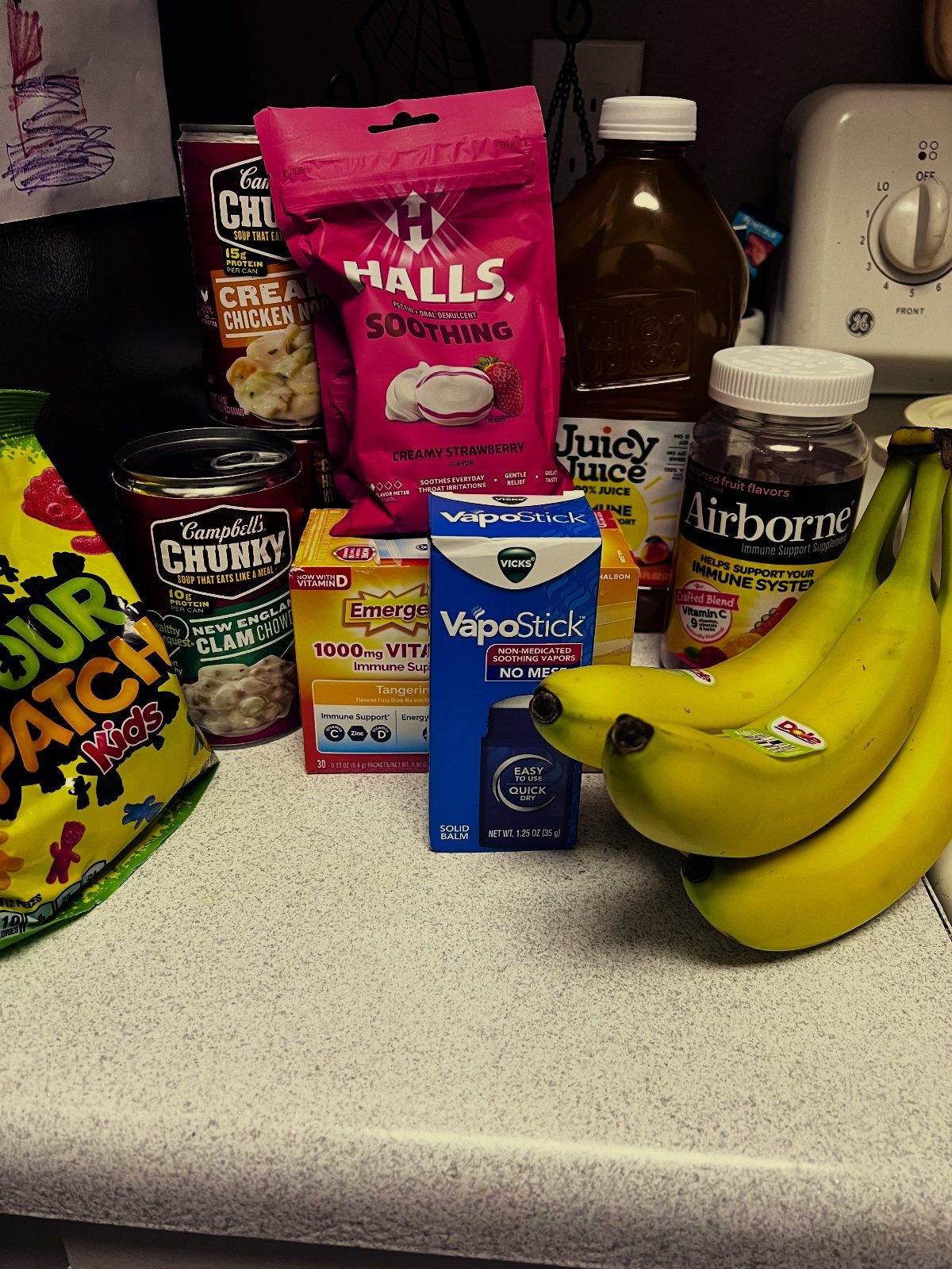 Assorted get well items including soup, cough drops, vitamins, and bananas on a counter.
