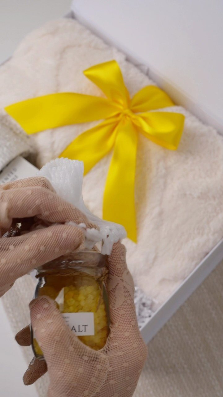 Hands in dotted gloves holding a jar next to a white gift box.