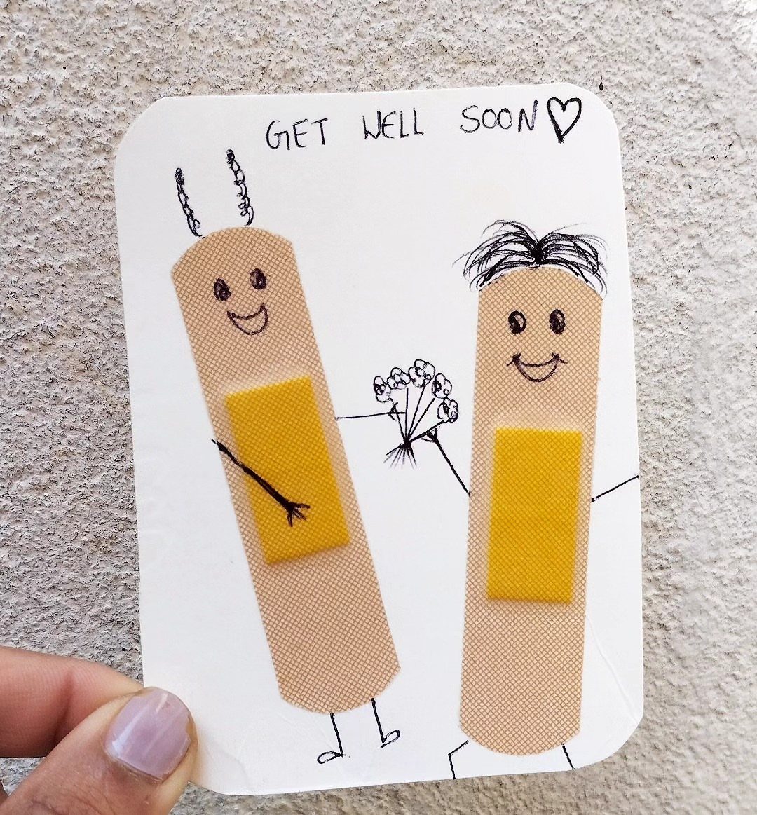 Handwritten get well soon card featuring two cute adhesive bandage characters holding flowers.