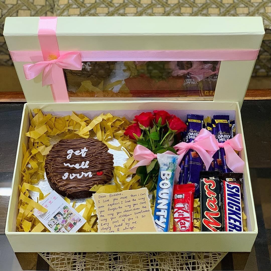 Gift box with get well soon cake, red roses, chocolates, and handwritten note.