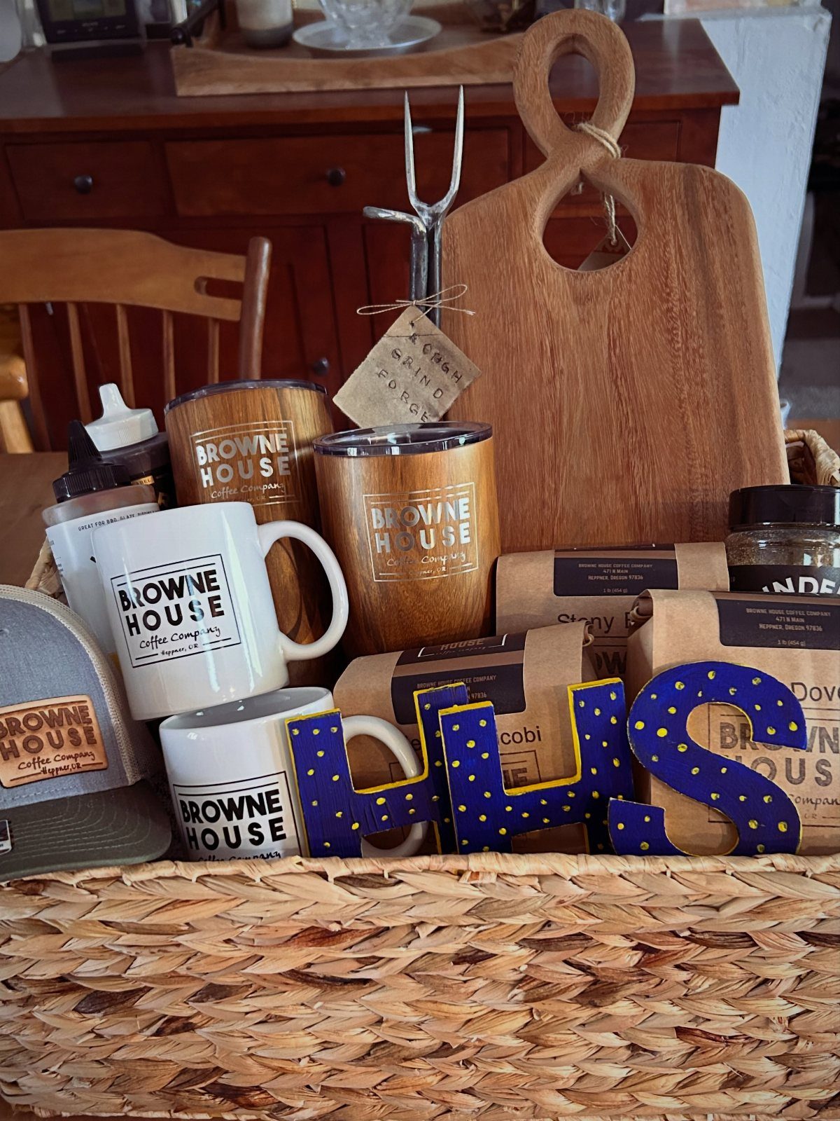 Woven gift basket containing coffee mugs, coffee bean bags, and a wooden board.