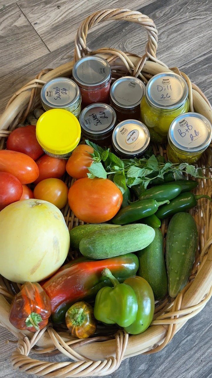 Woven basket filled with fresh garden vegetables and jars of homemade preserves.