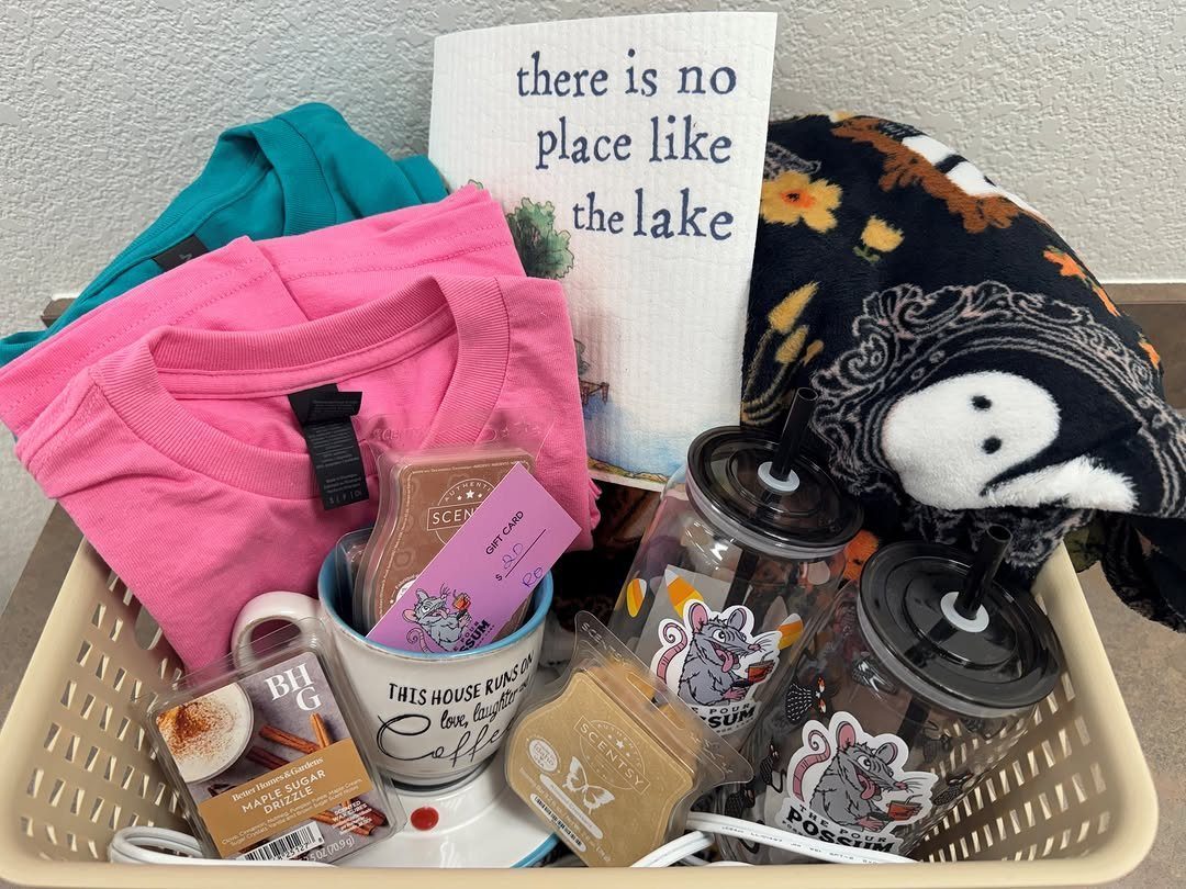 Gift basket containing a pink shirt, lake-themed sign, mug, and cozy blanket.