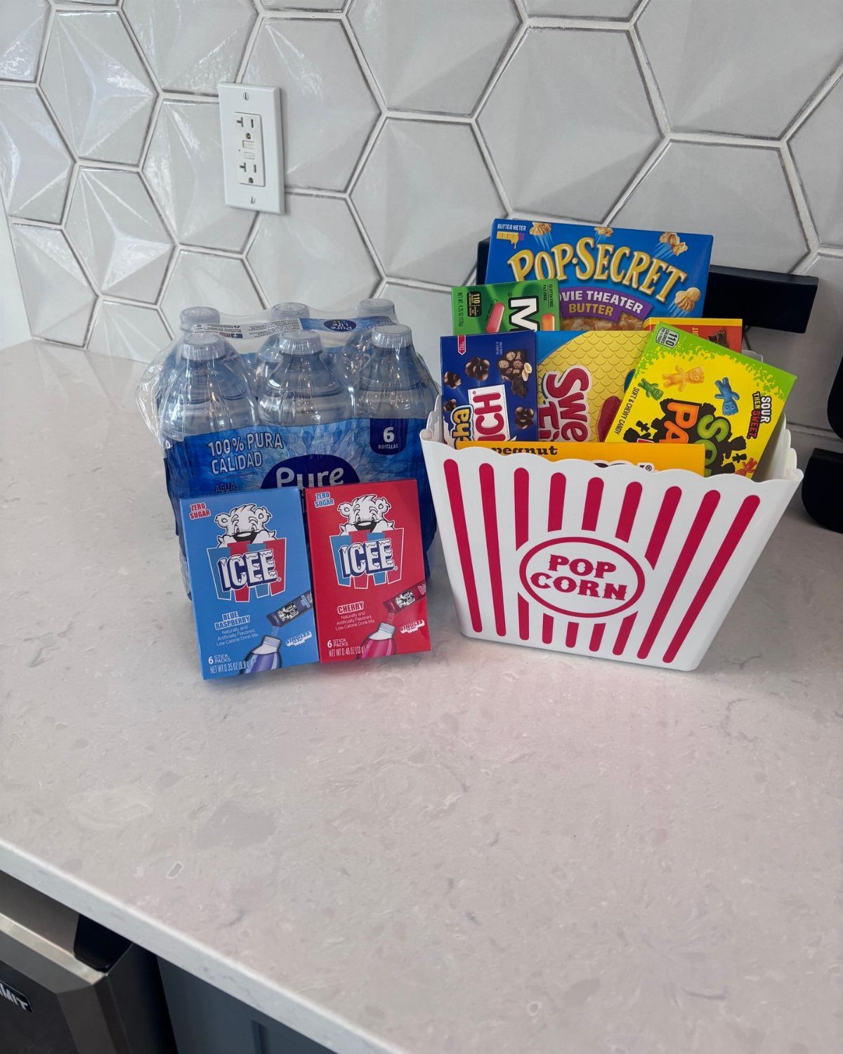 Movie night gift basket with popcorn, candy, and drinks on a white counter