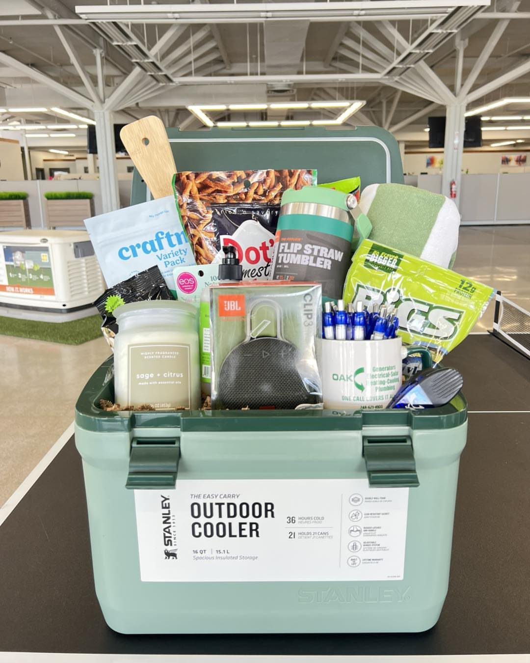 Light green outdoor cooler filled with snacks, electronics, and gear for a gift basket.
