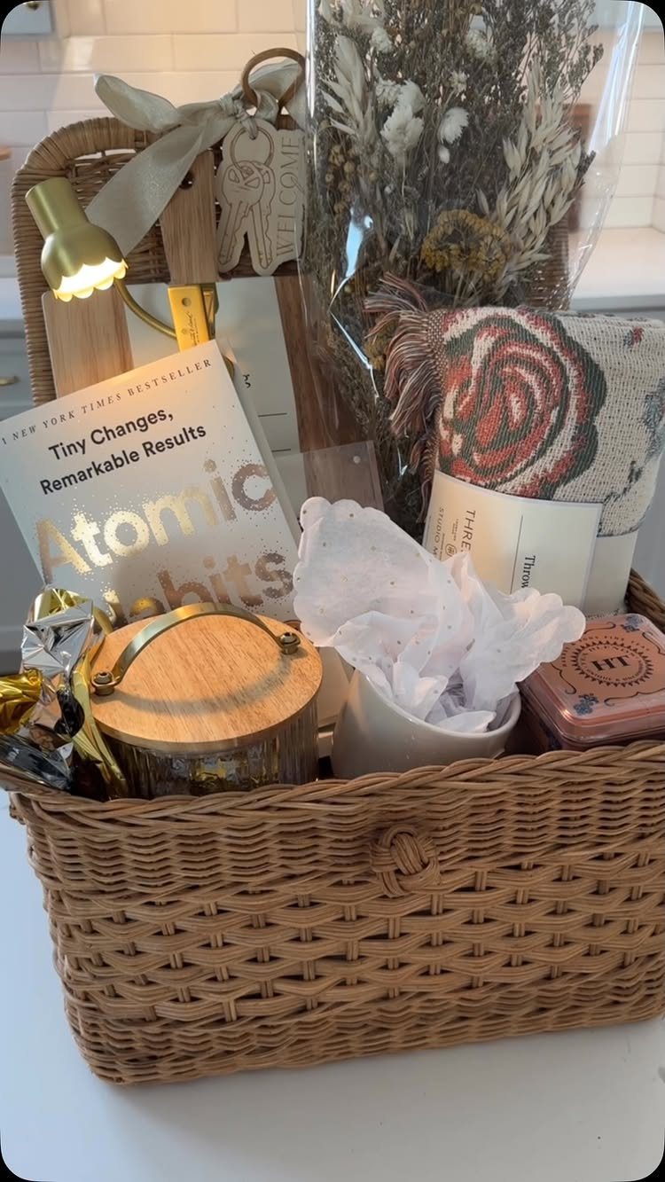 Woven wicker gift basket containing a book, dried flowers, and a cozy blanket.