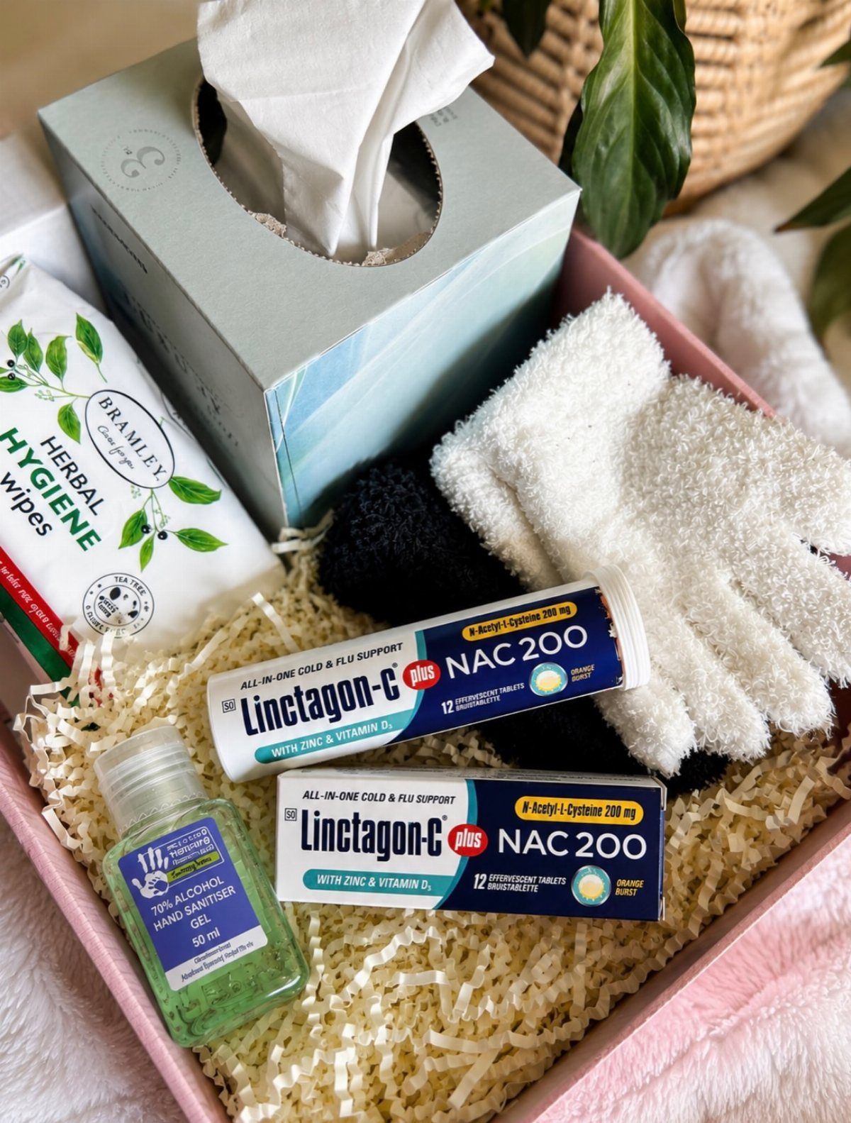 Care package in a pink box with tissues, medication, wipes, and fluffy socks.