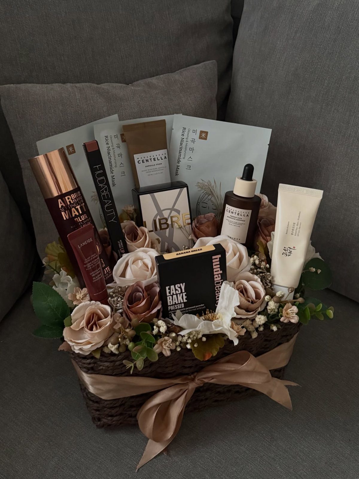 Cosmetic gift basket with makeup and skincare products surrounded by artificial roses.