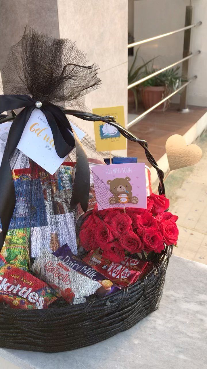 Wicker gift basket filled with assorted chocolates, candies, and red roses with black bow.