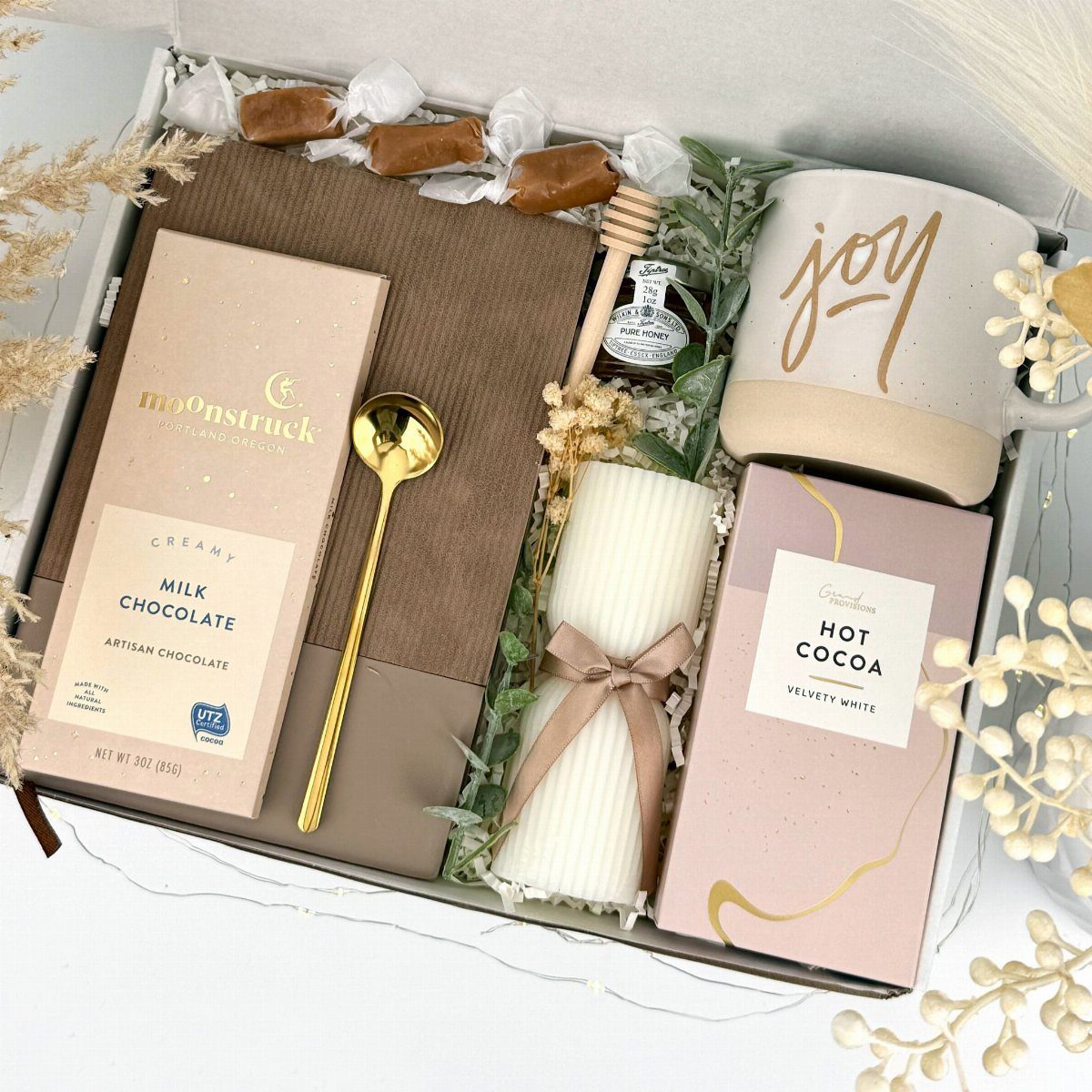 Gift box with hot cocoa, milk chocolate, a white candle, and a joy mug.