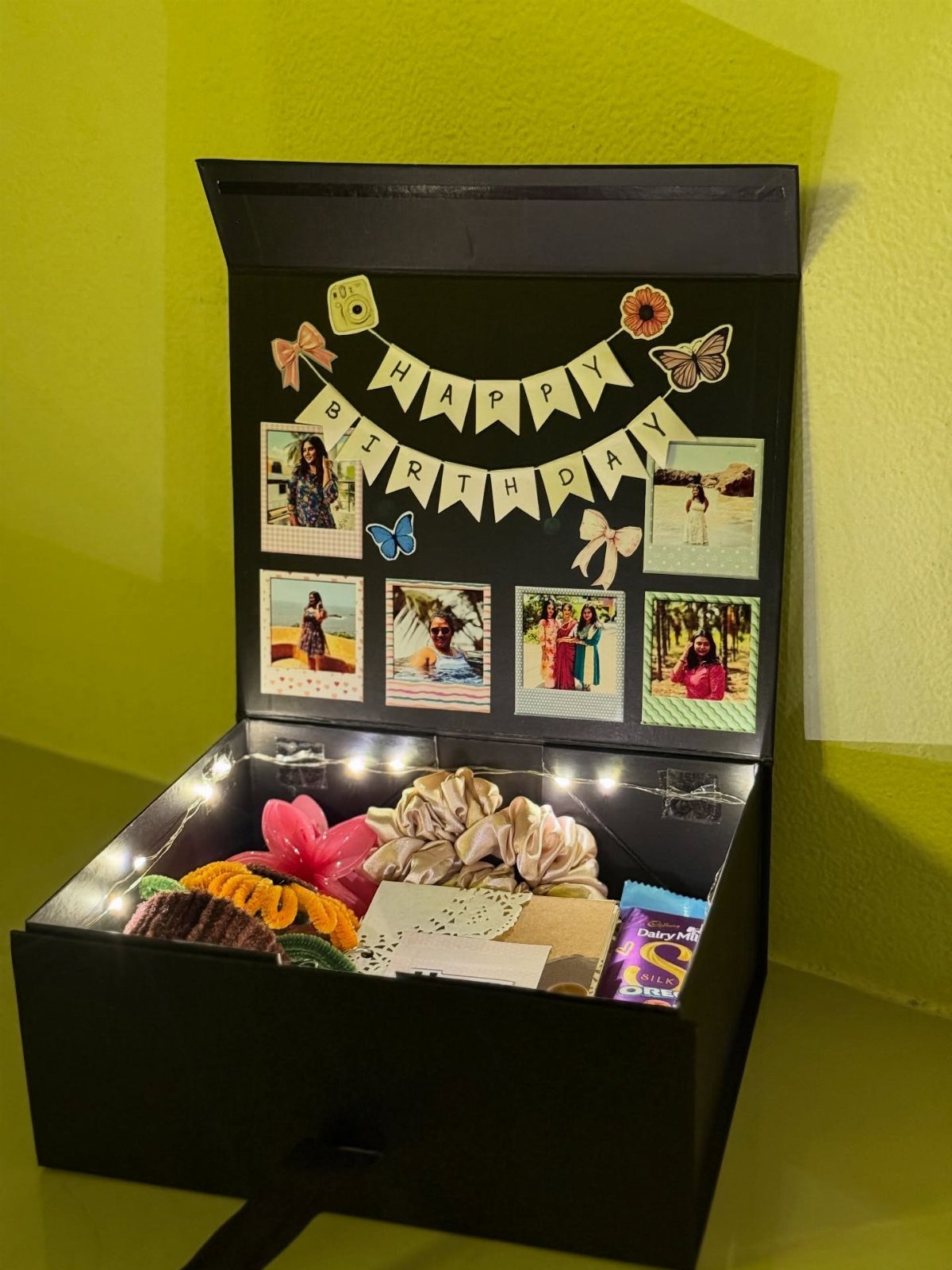 Black gift box with birthday photos on lid and various small gifts inside.