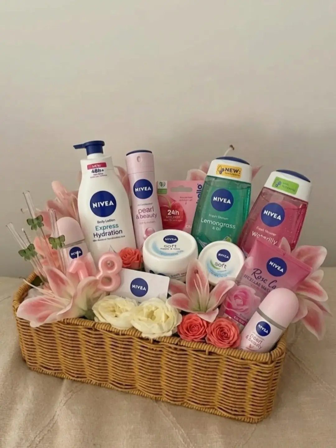 Wicker gift basket filled with Nivea skincare products and pink artificial flowers.