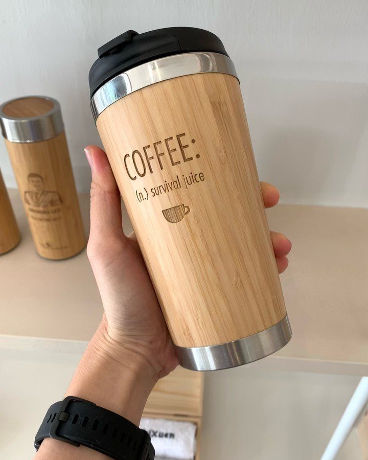 Bamboo travel mug with coffee survival juice text held in a hand