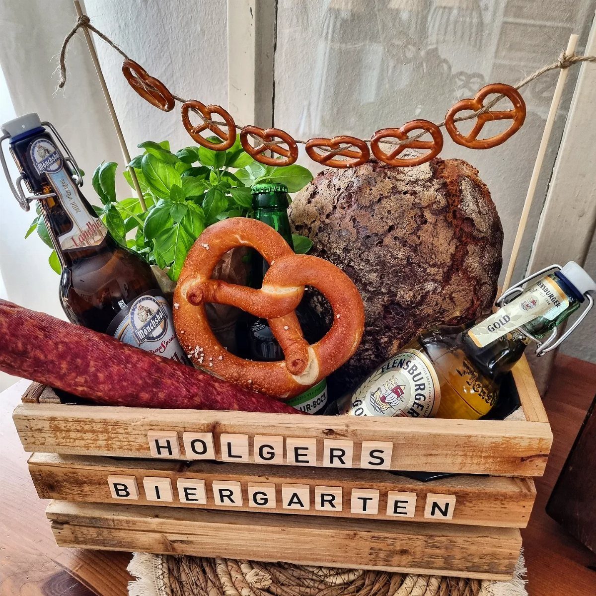 Wooden beer garden crate with beer bottles, pretzels, rustic bread, and salami sausage.