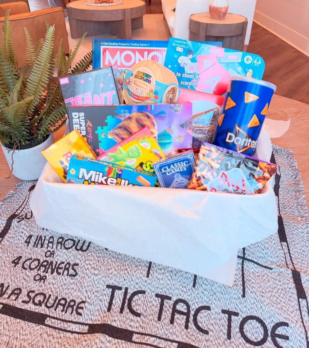 White gift basket filled with board games and snacks on a game-themed rug.