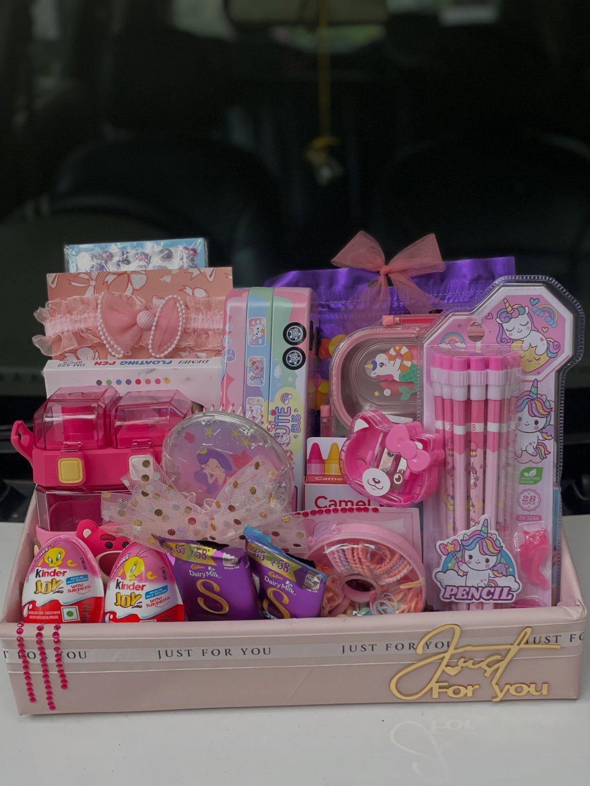 Pink gift tray filled with unicorn stationery, pink pencils, and Kinder Joy chocolates.