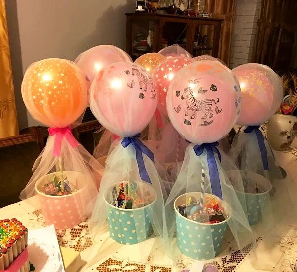 Colorful treat buckets with balloons and tulle ribbons on a lace tablecloth.