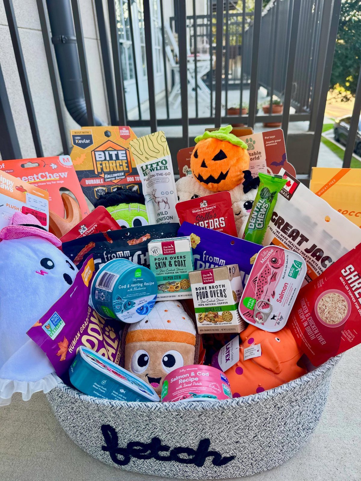 Grey fabric basket filled with dog treats, toys, and pet supplies for dogs.