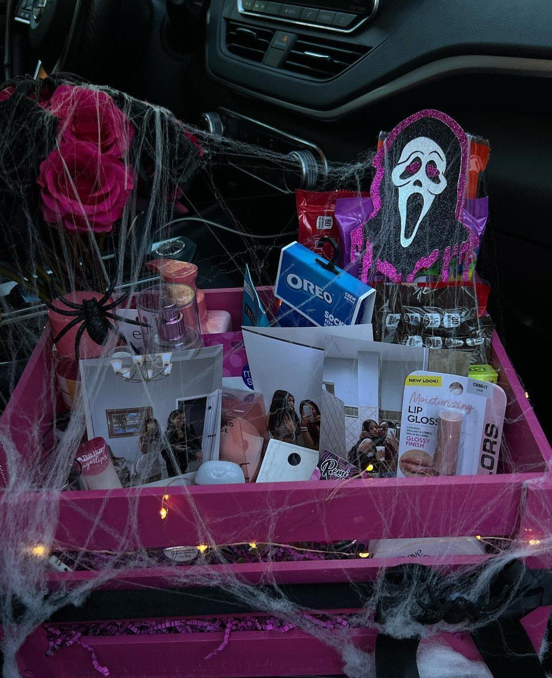 Pink gift crate with snacks and cosmetics decorated with spooky Halloween spider webs.