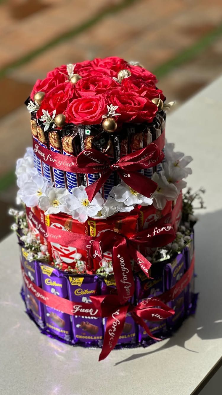 Chocolate bar cake decorated with red roses, white flowers, and red ribbons.