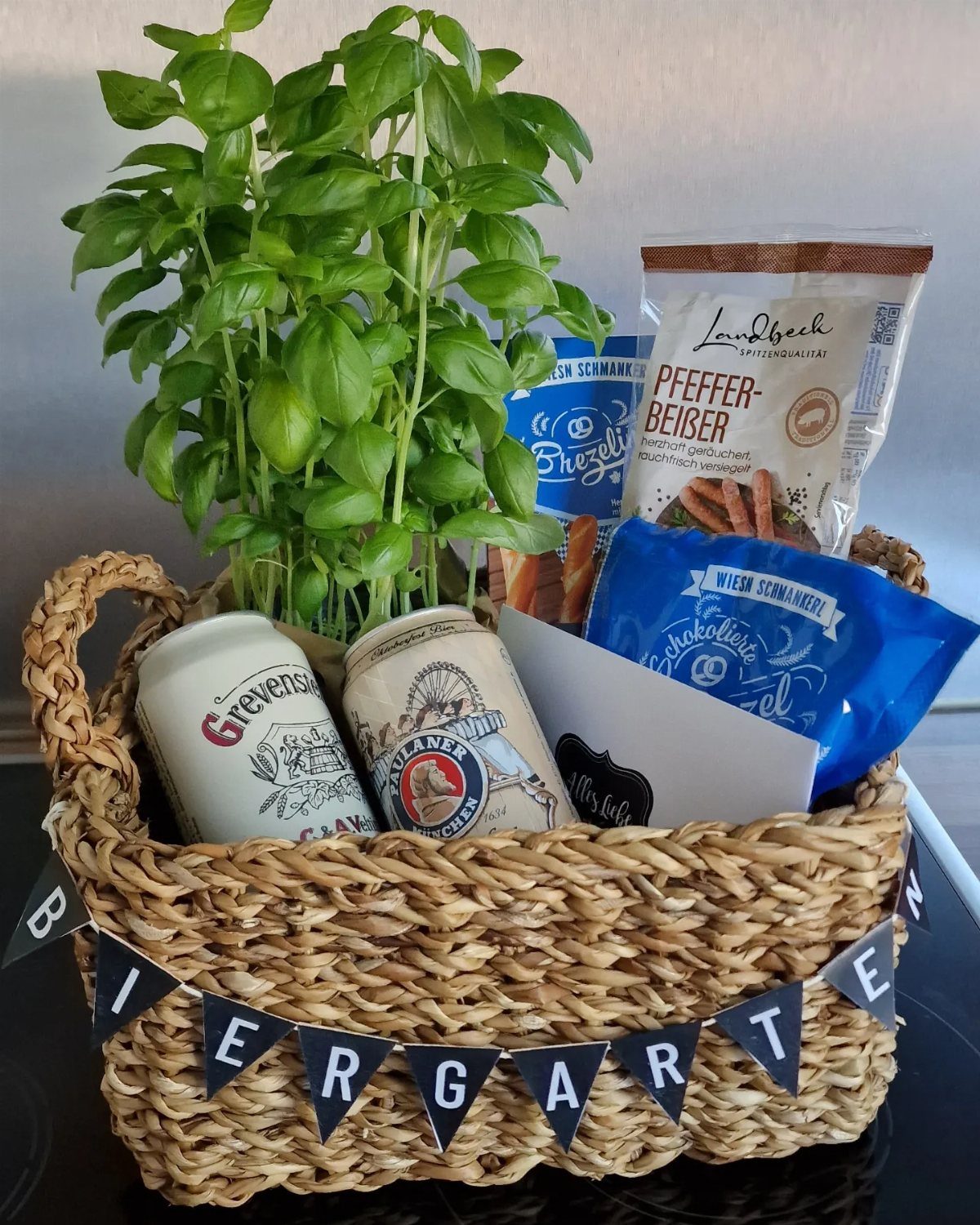 Woven gift basket with beer cans, snacks, and a basil plant for beer lovers.