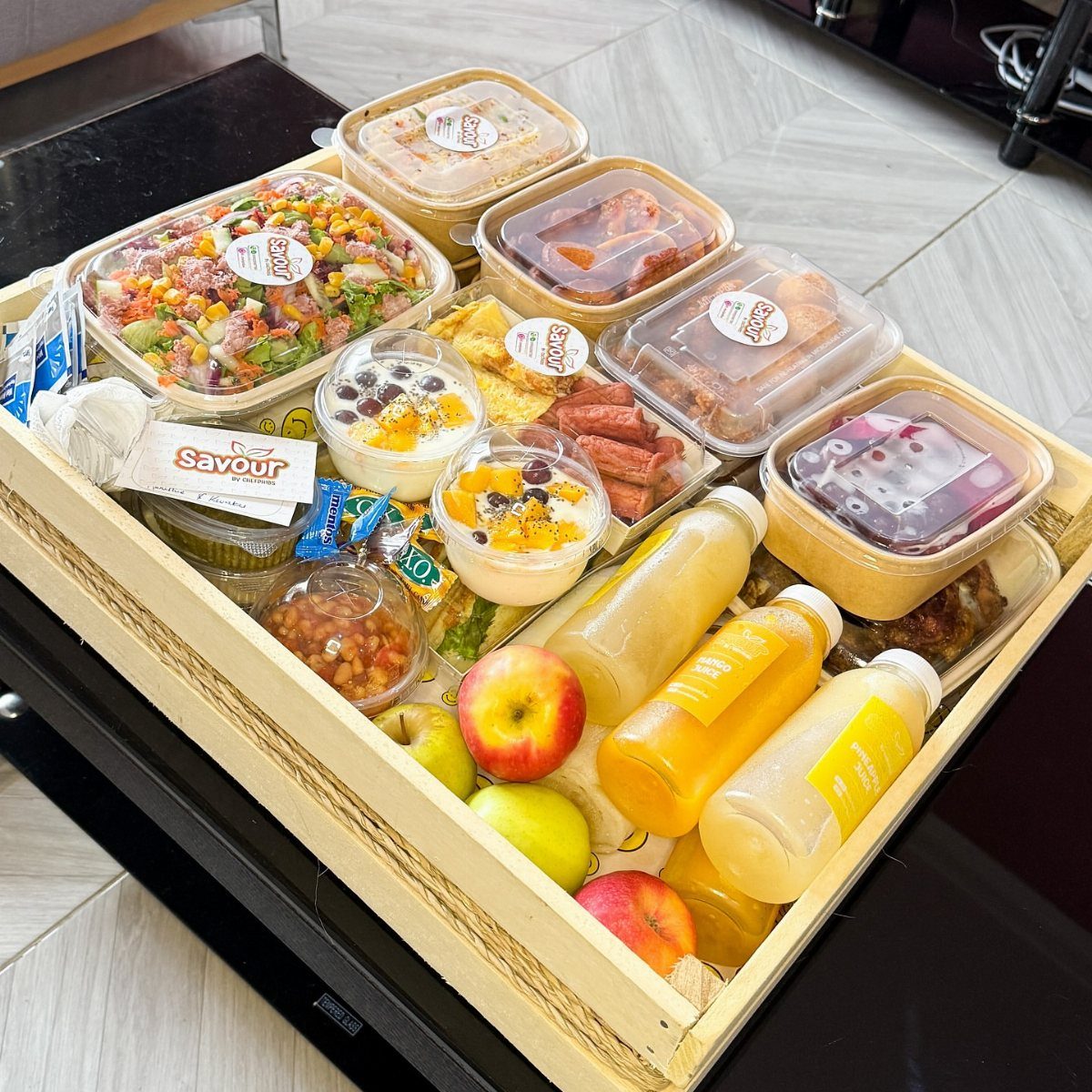 Wooden crate filled with gourmet salads, meats, fresh fruit, and bottled juices.