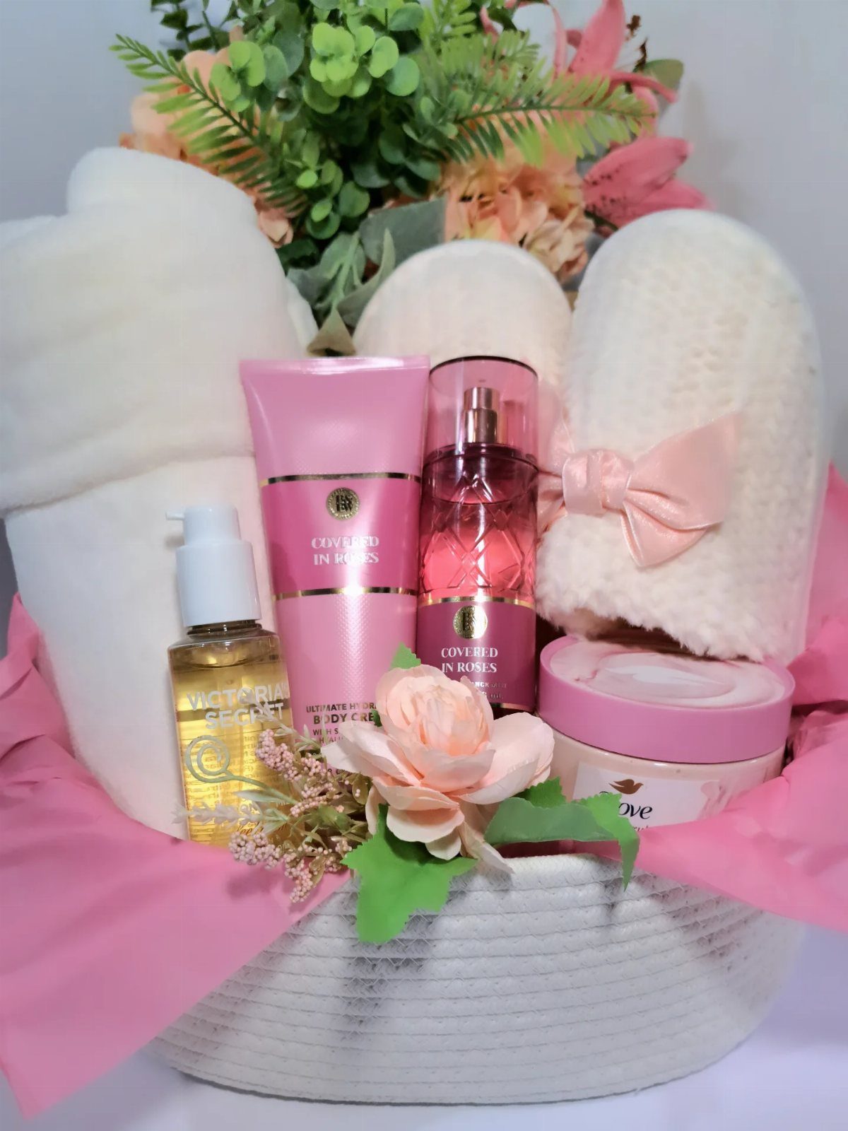 Personal care gift basket with pink lotions, fragrance, white towels, and peach flower.
