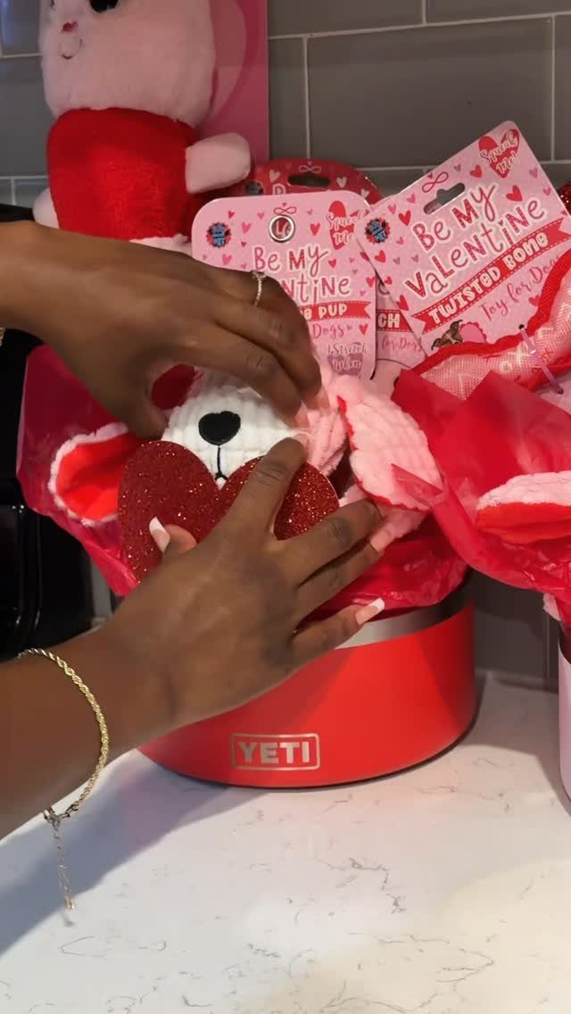 Hands arranging a red Yeti cooler filled with Valentine's Day pet treats and toys.
