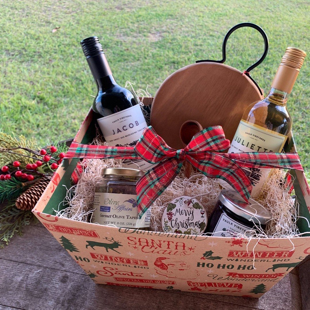Holiday gift basket with two wine bottles, wooden board, and gourmet jars.