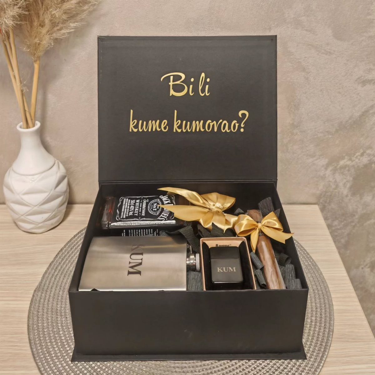 Black gift box with a cigar, silver flask, and gold ribbon on a table