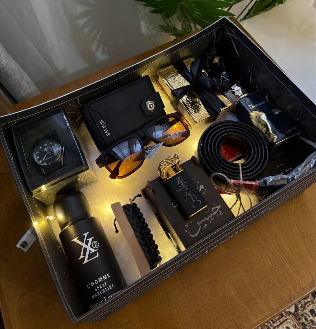 Black gift box with watch, wallet, sunglasses, and belt illuminated by fairy lights.