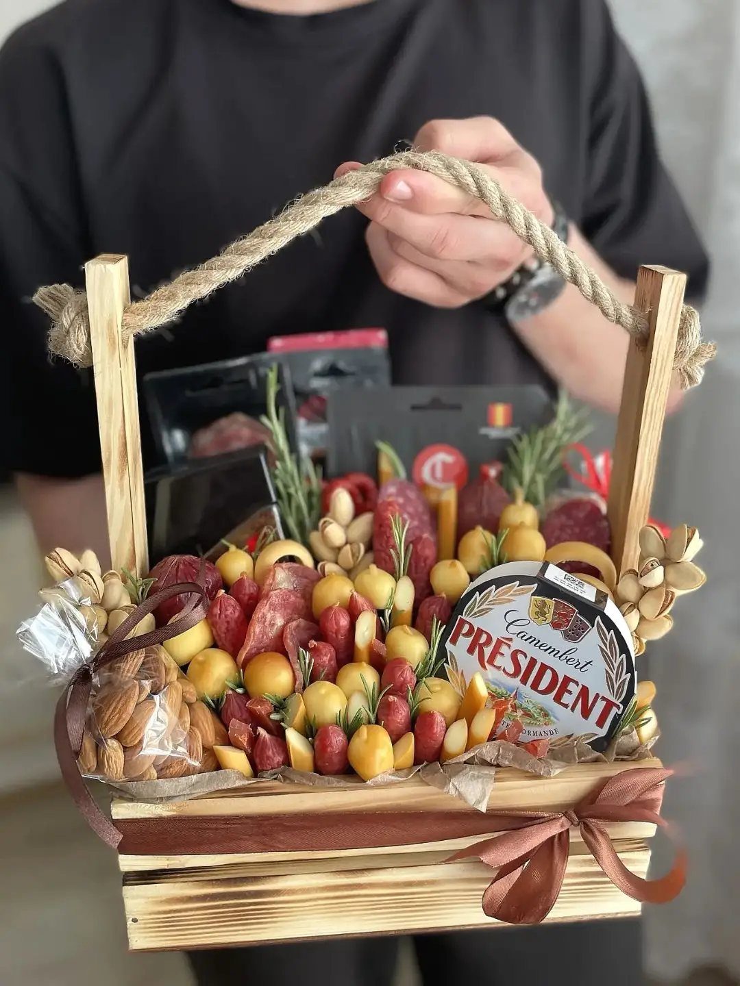 Wooden gift crate filled with assorted cured meats, cheeses, and nuts held by person