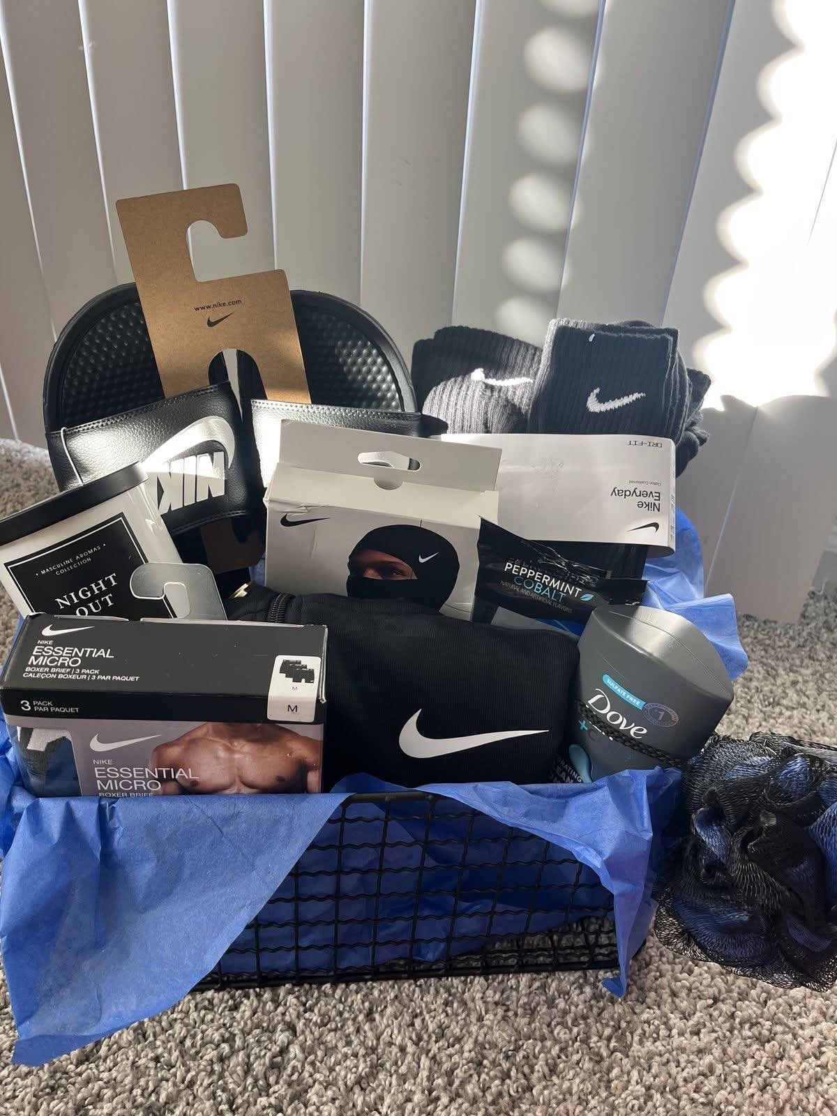 Black wire gift basket with Nike apparel, grooming products, and blue tissue paper.
