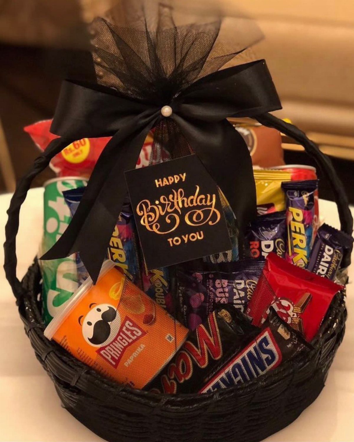 Black wicker gift basket filled with assorted chocolates and chips with a birthday card.