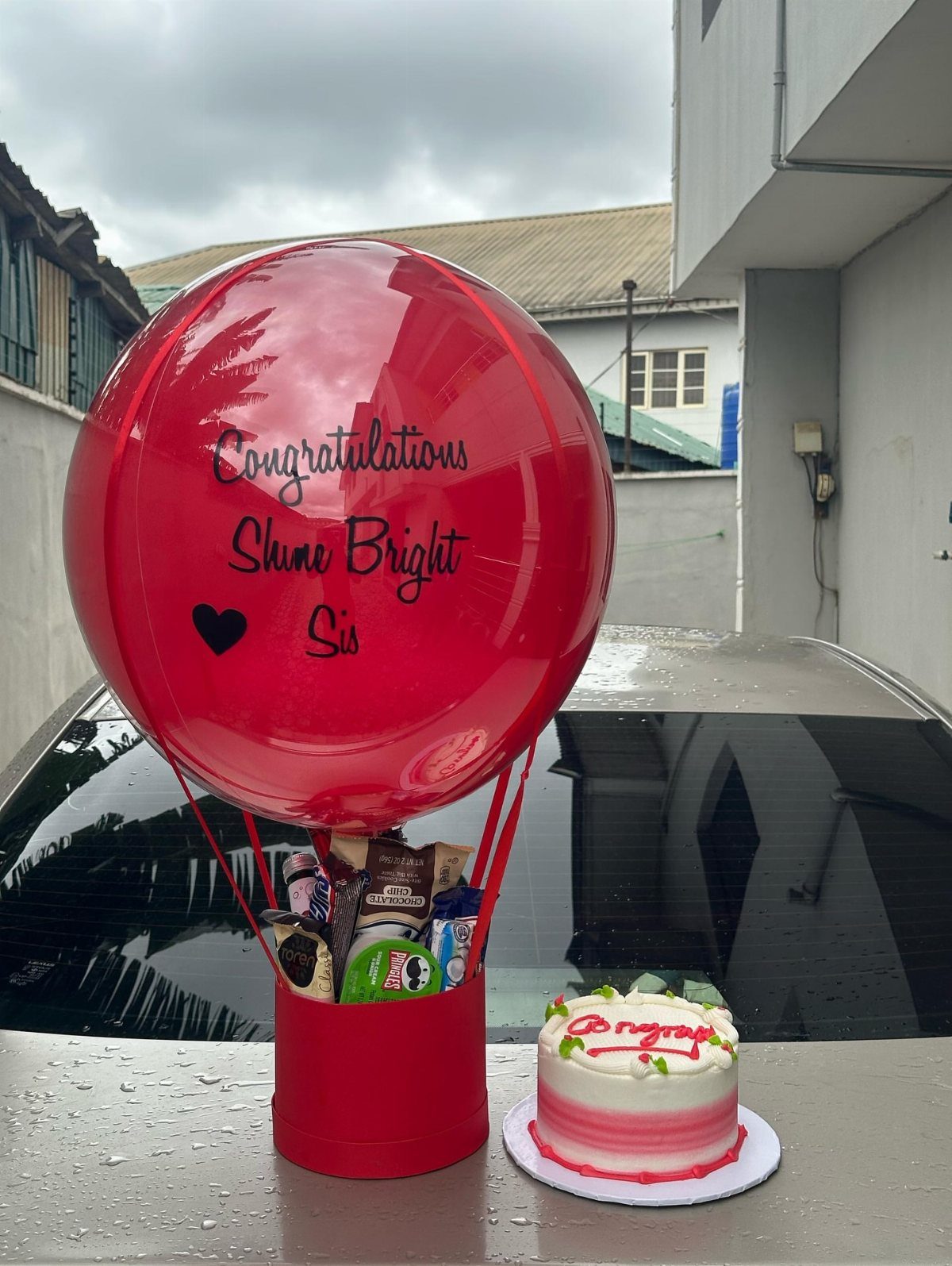 Red hot air balloon gift basket with snacks and a small celebratory cake.