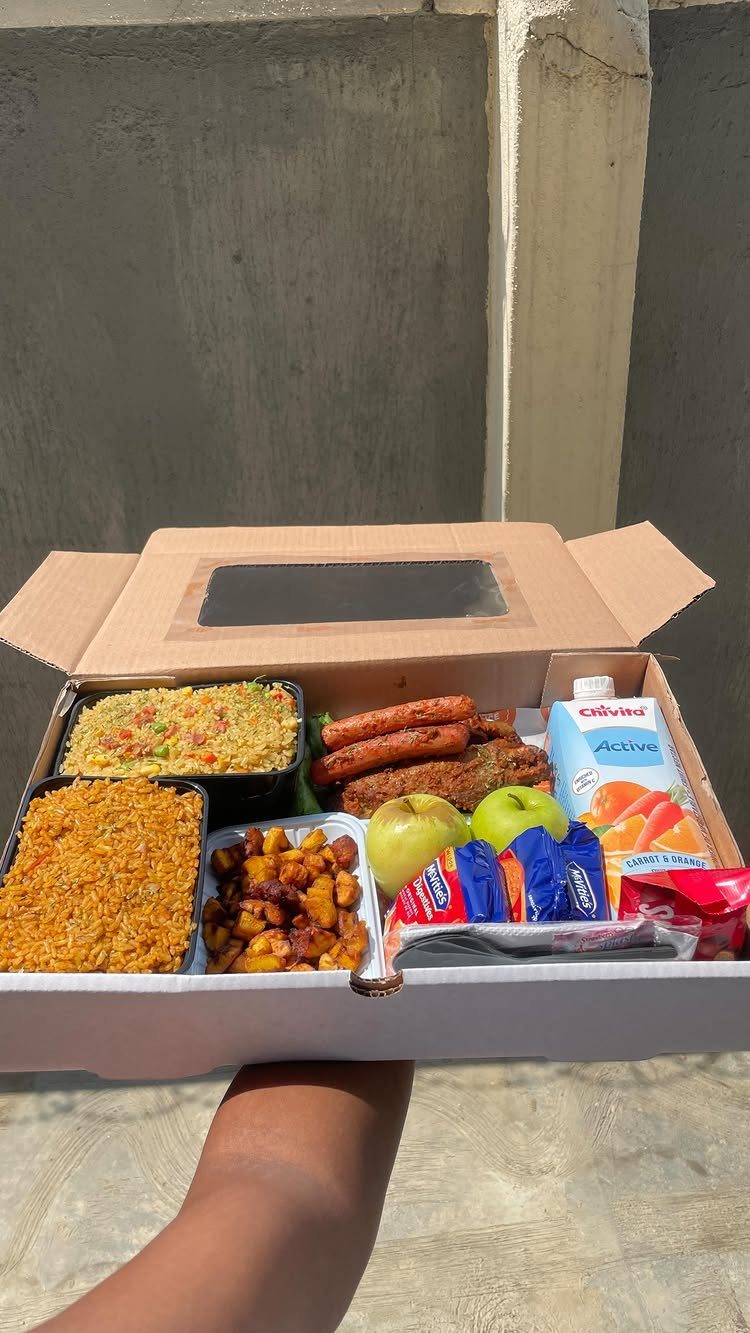 Cardboard food box filled with rice, plantains, sausages, apples, and milk.