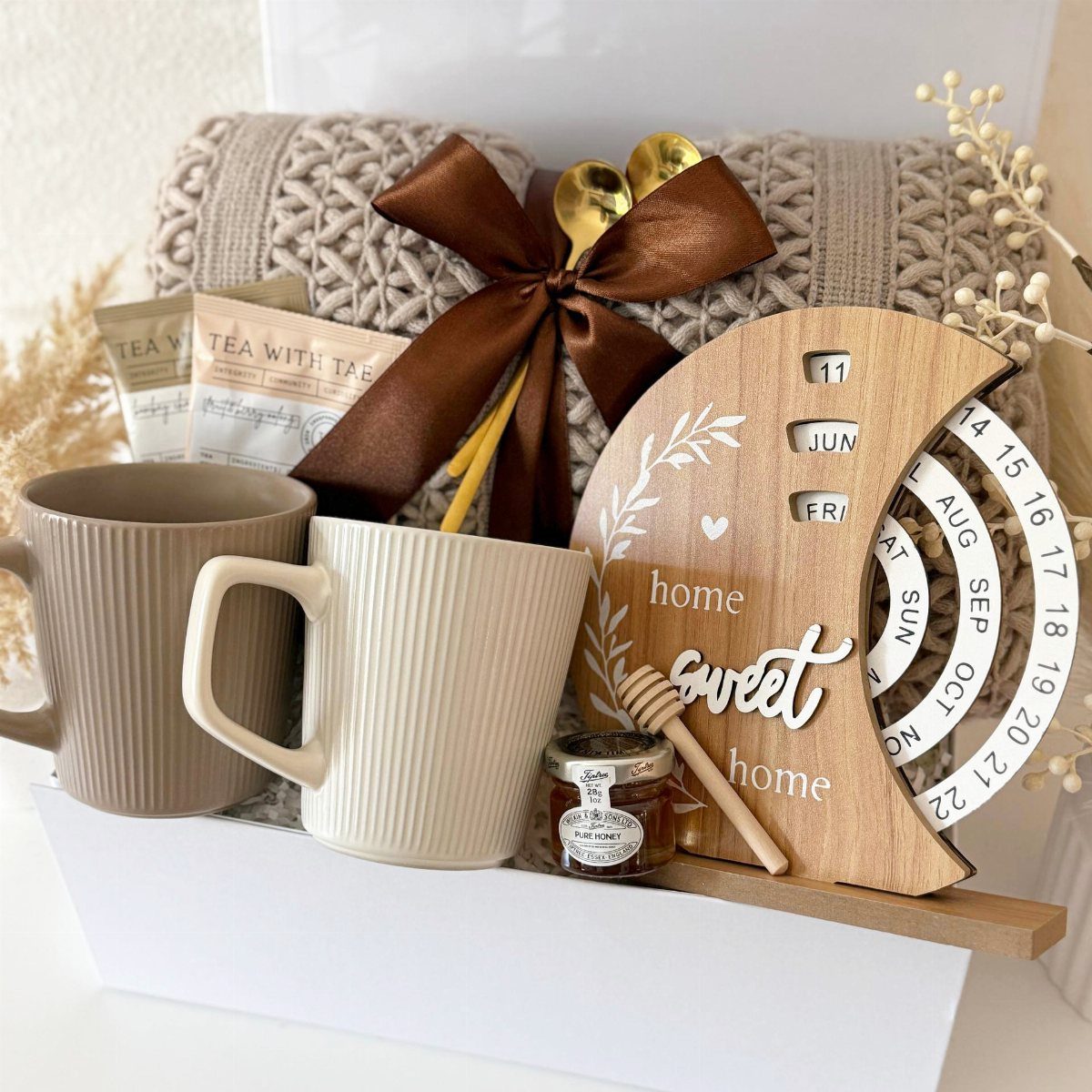 Housewarming gift box with mugs, honey, a knit blanket, and home sweet home sign.