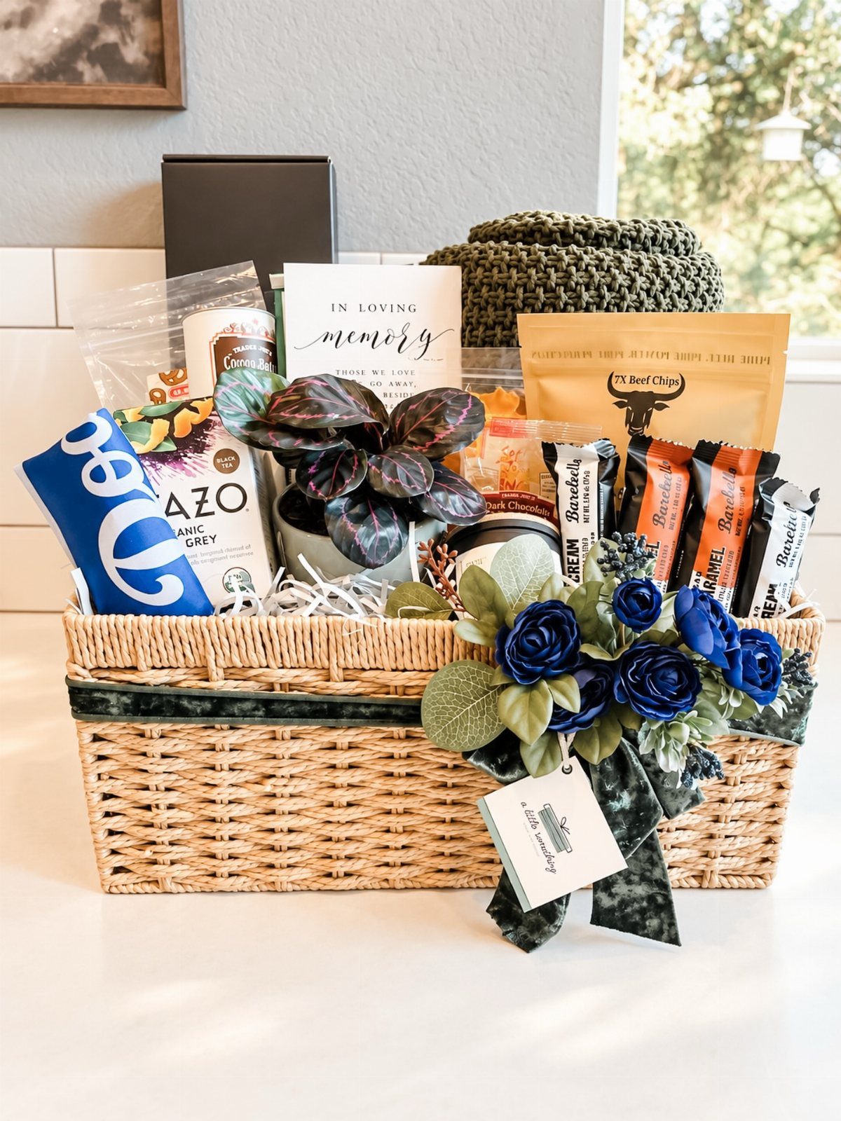 Woven gift basket with snacks, a plant, and an In Loving Memory card.