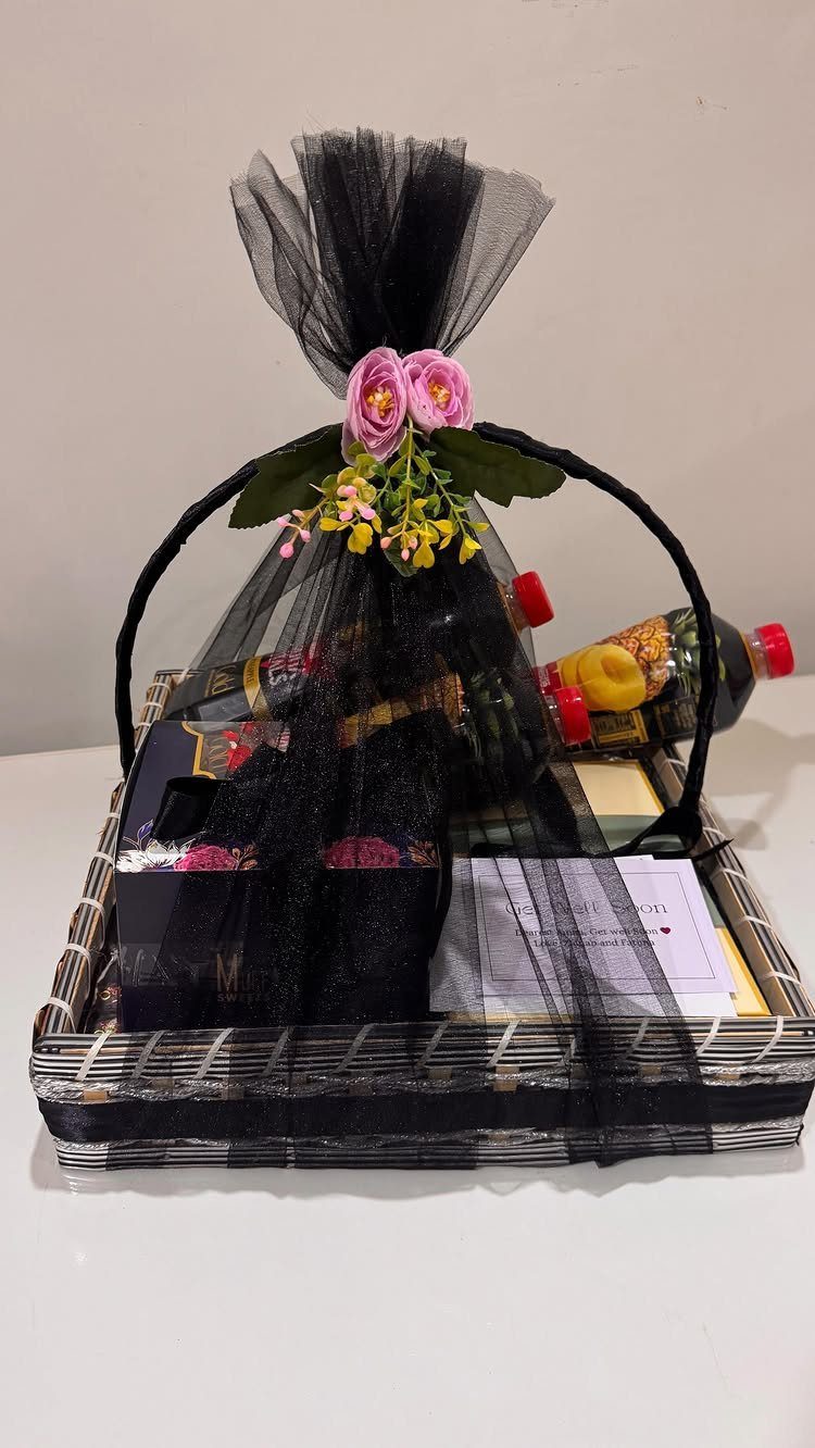 Woven gift basket wrapped in black tulle with pink and yellow floral accents.