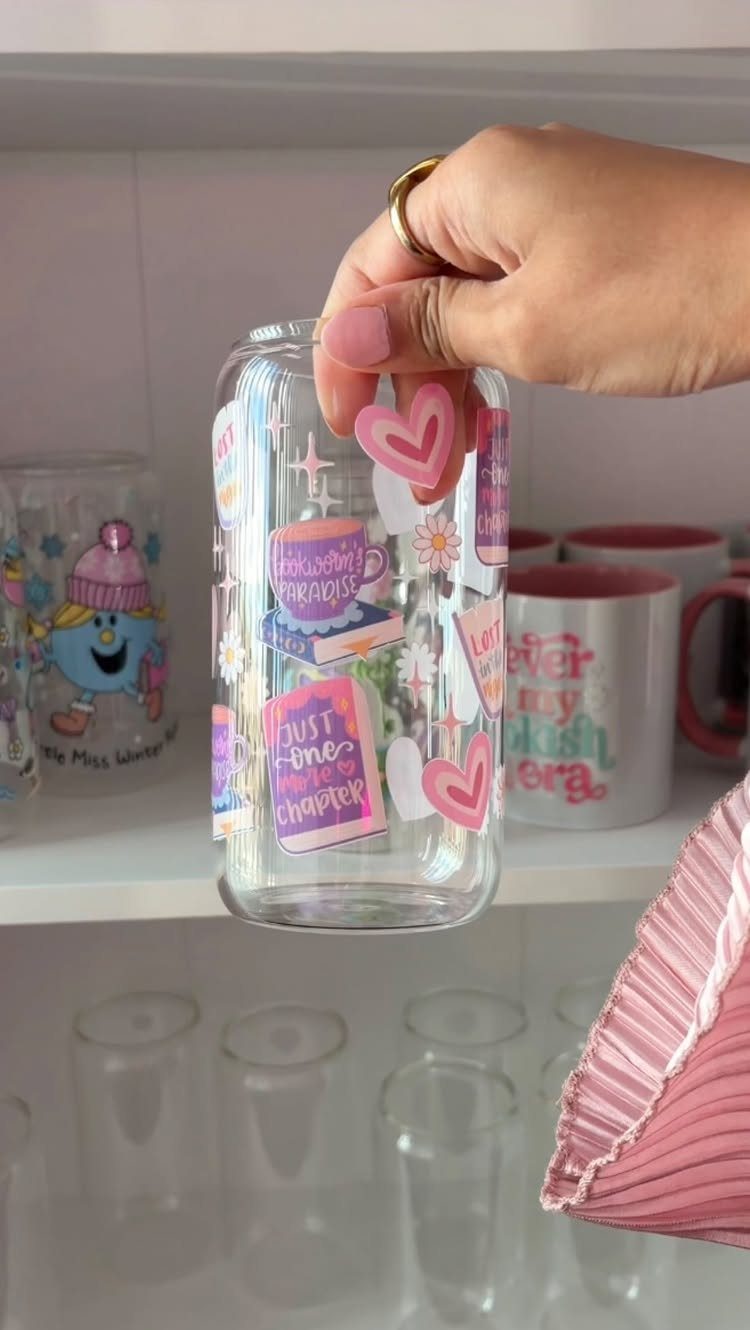 Decorated glass bottle with colorful stickers held by a hand against white shelving.