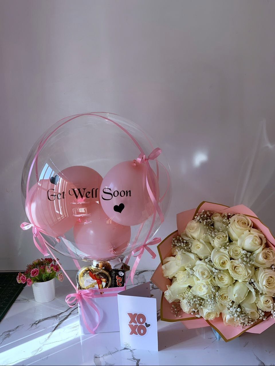 Get well soon balloon with pink balloons, white roses, and a greeting card.