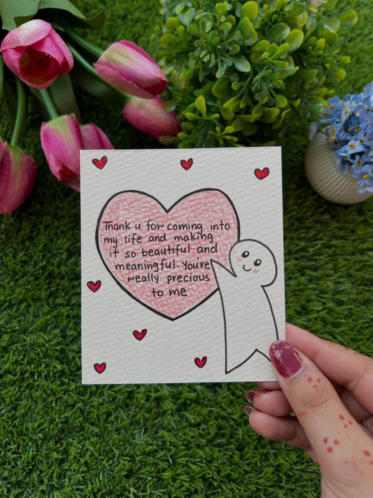 Handwritten note with a pink heart and character held against pink tulips.