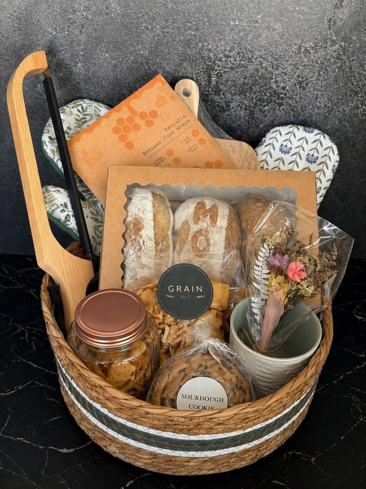 Woven gift basket filled with artisanal bread, cookies, and a jar of preserves.