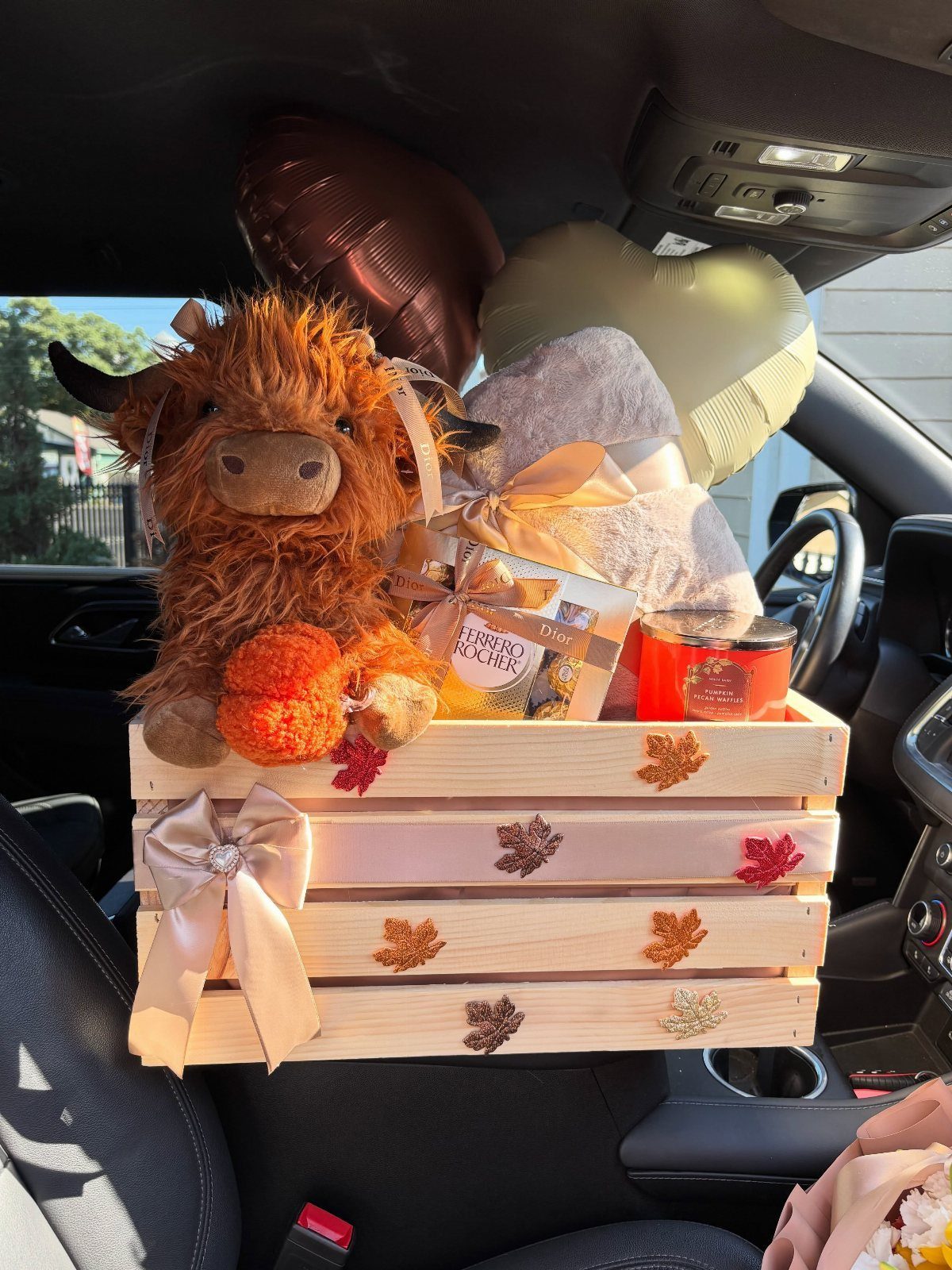 Autumn themed gift crate with a highland cow plush and decorative pumpkins in a car
