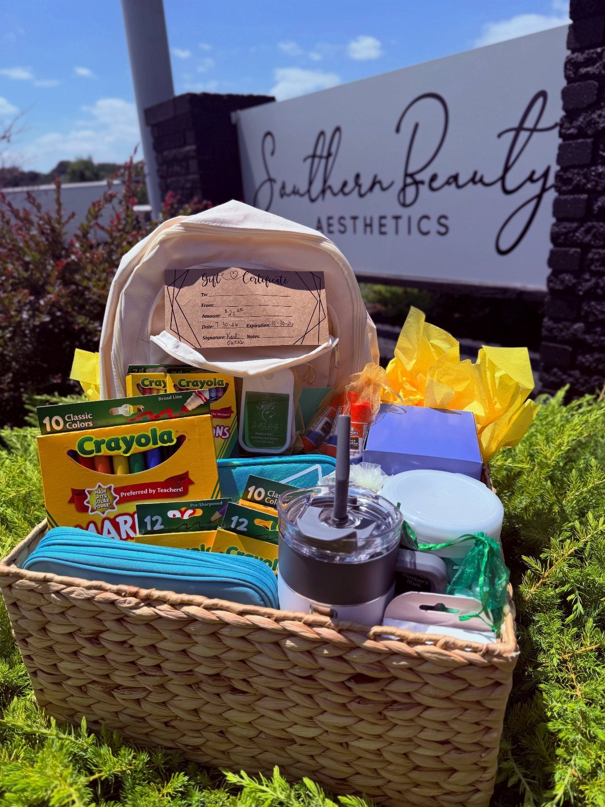 Woven basket filled with crayons, a backpack, and school supplies on green grass.