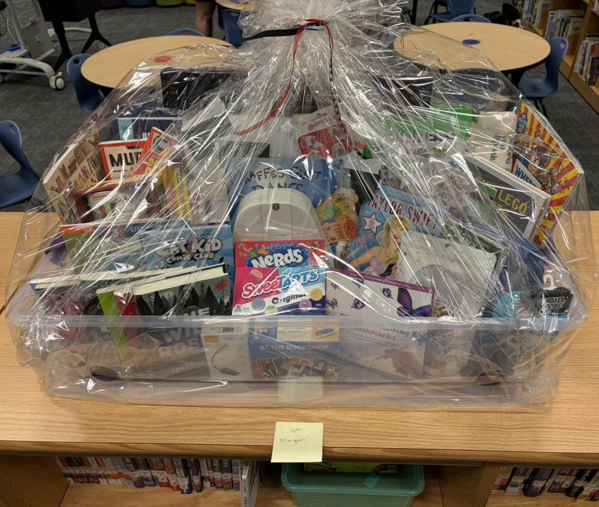 Gift basket with books and candy wrapped in clear cellophane on a table.